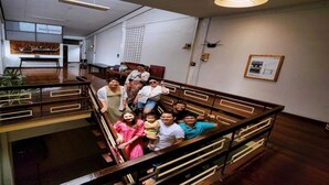 A group of people on a wooden staircase inside a building with a modern interior, including a dining area with a wooden table and chairs, and a wall-mounted light fixture. - Baan Kong Hostel (Takua Pa)