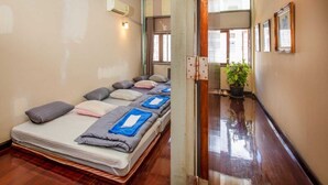 A hotel room with a long bed, a potted plant, and a hallway with framed pictures. - Baan Kong Hostel (Takua Pa)