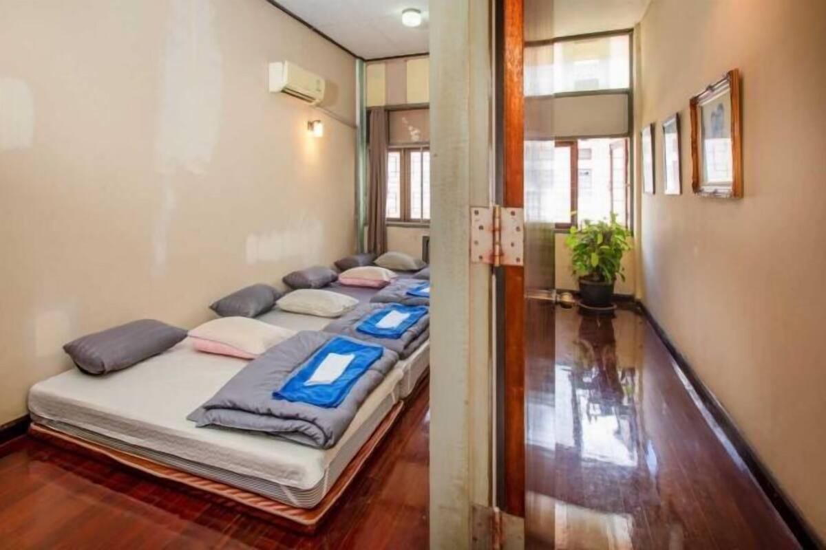A hotel room with a bed, pillows, a potted plant, and a hallway with a mirror and framed pictures.