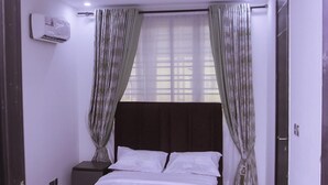 A bedroom with a bed, curtains, an air conditioning unit, and a door. - Stunning 3-bed House in Lagos (Lagos)