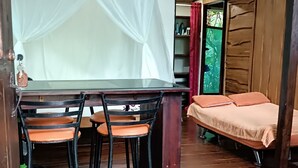 Ein Zimmer mit Holzboden, einem Bett mit orangefarbener Bettwäsche, einem Tisch und zwei Stühlen sowie einem Ventilator.