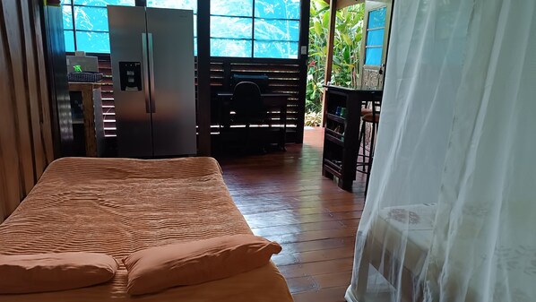 A room with a bed, a refrigerator, and a window with a view of greenery.