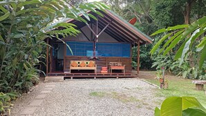 Eine Holzhütte mit einer Veranda, zwei Holzbanken mit Kissen und einem Hängesessel.