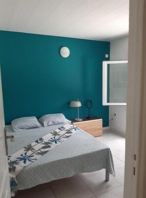 Une chambre avec un mur d’accent de couleur turquoise, un lit recouvert d’une couvre-lit à motifs floraux, une table de chevet avec une lampe et une fenêtre.