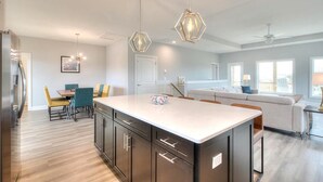Una cocina moderna con una isla central, zona de comedor con sillas y sala de estar con sofá y ventanas.