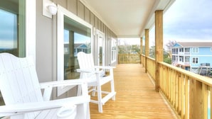 Una terraza de madera con sillas Adirondack blancas y vistas a casas al fondo.