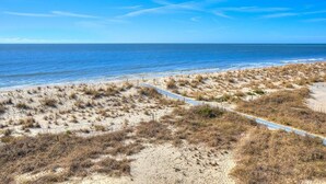 Ein Strand mit einem sandigen Pfad, der zum Wasser führt, umgeben von Dünen.