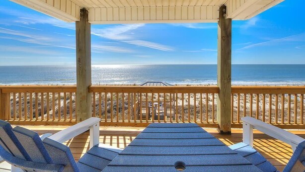 Eine Holzterrasse mit Liegestühlen mit Blick auf einen Strand.