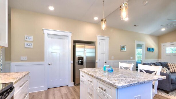 A modern kitchen with white cabinetry, a granite countertop island, stainless steel appliances, and pendant lighting. - Captain Jacks: Cozy 3BR Oak Island retreat, perfect for family fun and relaxation. (Oak Island)