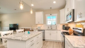 A modern kitchen with white cabinetry, granite countertops, a built-in oven, and a large window providing natural light. - Captain Jacks: Cozy 3BR Oak Island retreat, perfect for family fun and relaxation. (Oak Island)