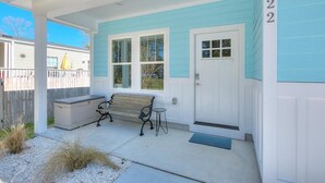 A covered porch with a bench, a small table, and a utility box. - Captain Jacks: Cozy 3BR Oak Island retreat, perfect for family fun and relaxation. (Oak Island)