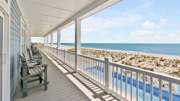 A covered porch with wooden chairs, a pool, and a beach view. - Experience beachfront luxury at Seaclusion, Oak Island's 10-bedroom retreat. (Oak Island)