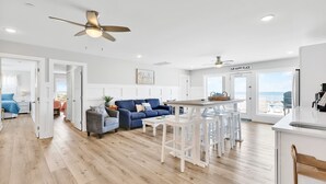 A spacious living area with a blue sofa, a coffee table, and a kitchen area with a bar stool. - Experience beachfront luxury at Seaclusion, Oak Island's 10-bedroom retreat. (Oak Island)