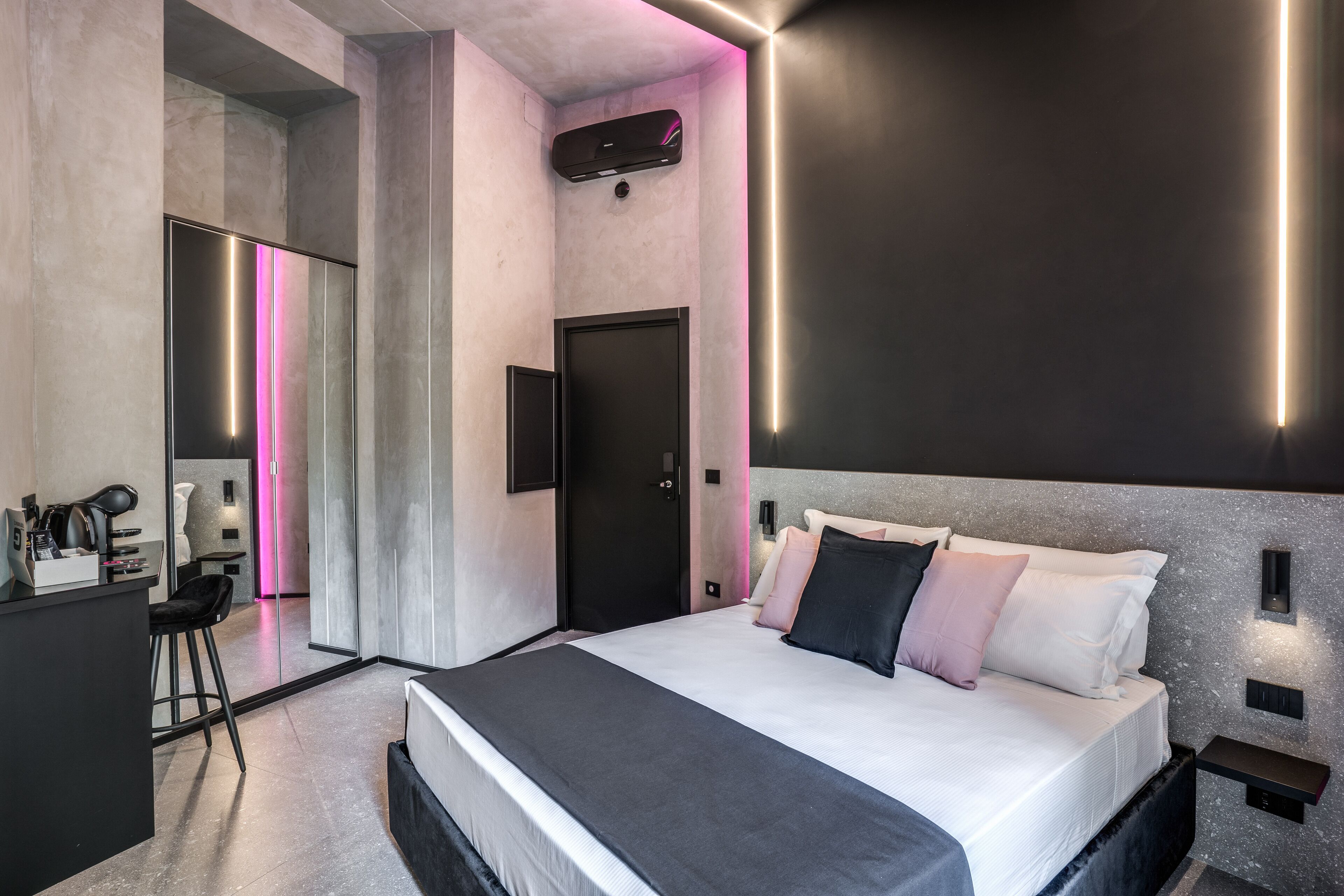 Una habitación de hotel moderna con una cama grande, un escritorio con silla y un baño visible a través de una puerta de vidrio.