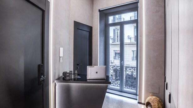 A modern interior with a black door, a laptop on a counter, and a view of buildings through a large window. - Gallery Experience Napoli (Naples)