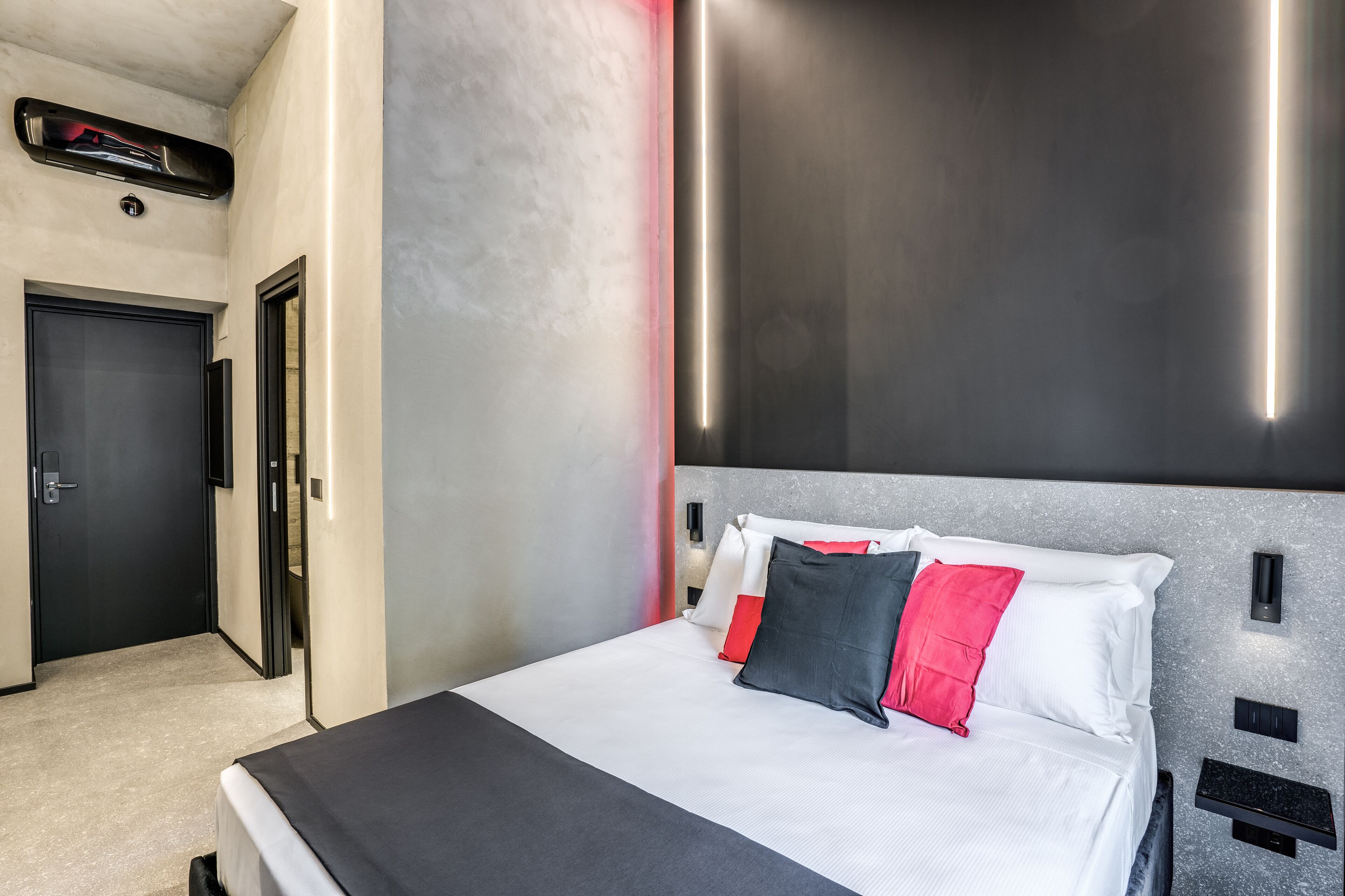 A modern hotel room with a large bed, a door, and a wall-mounted light fixture.