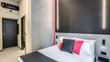 A modern hotel room with a large bed, a door, and a wall-mounted light fixture.