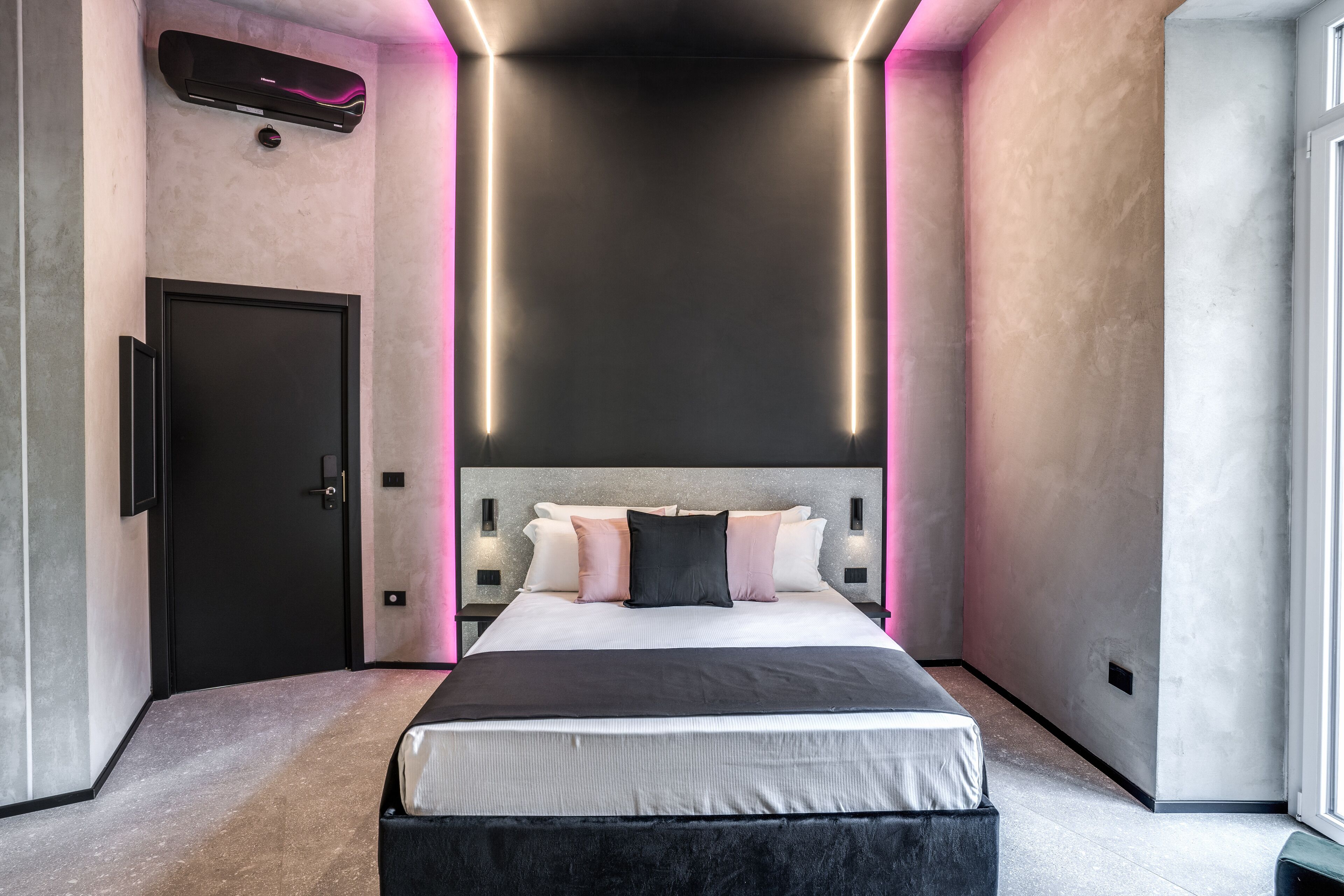 Quarto moderno com cama grande, porta escura e ar condicionado no teto.