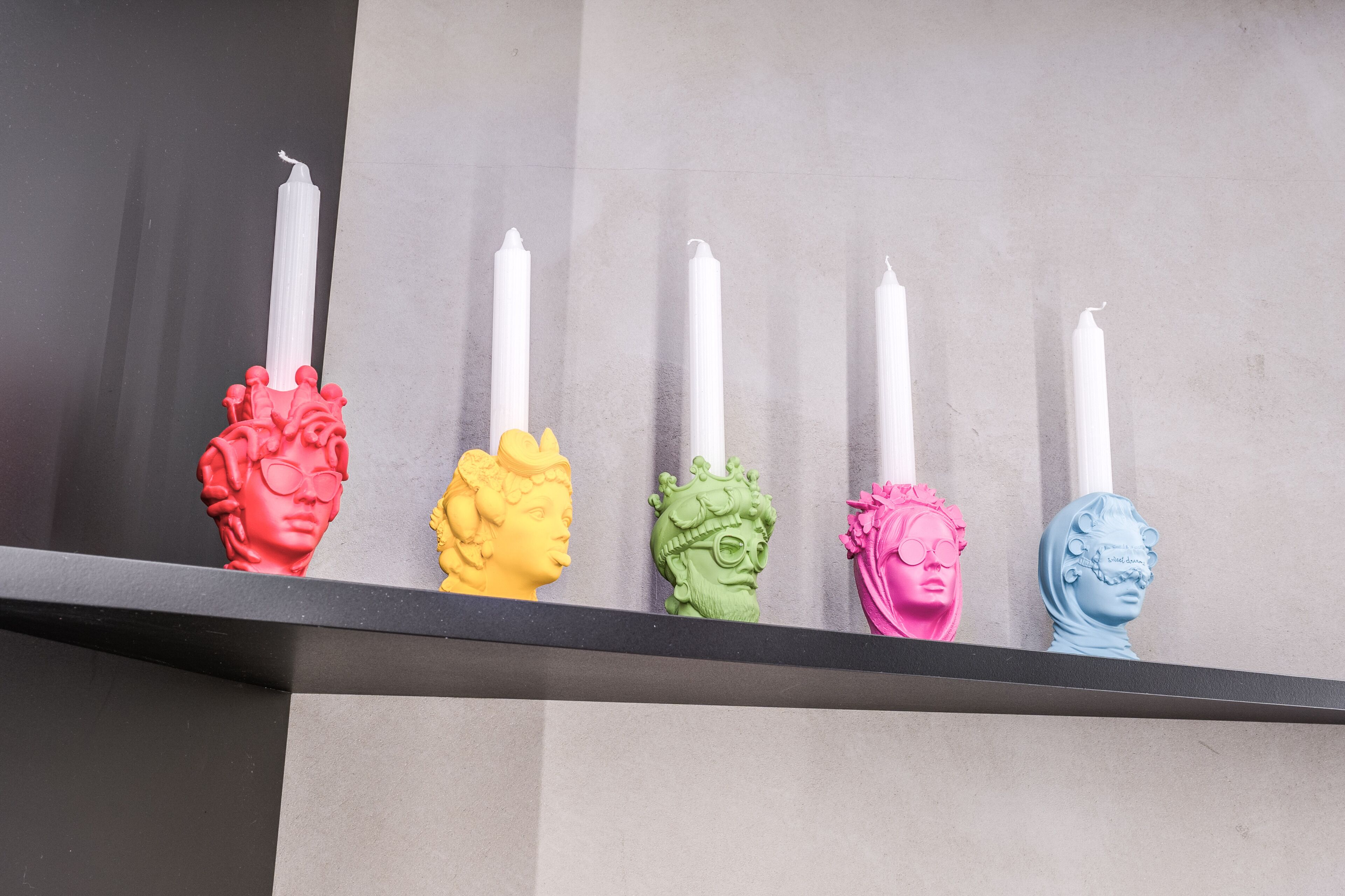 A shelf with five colorful busts and white candles.