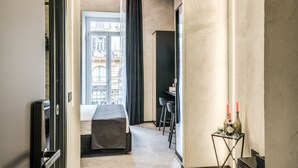 A hotel room with a bed, a desk, a chair, a small table with candles, and a view of a building outside. - Gallery Experience Napoli (Naples)