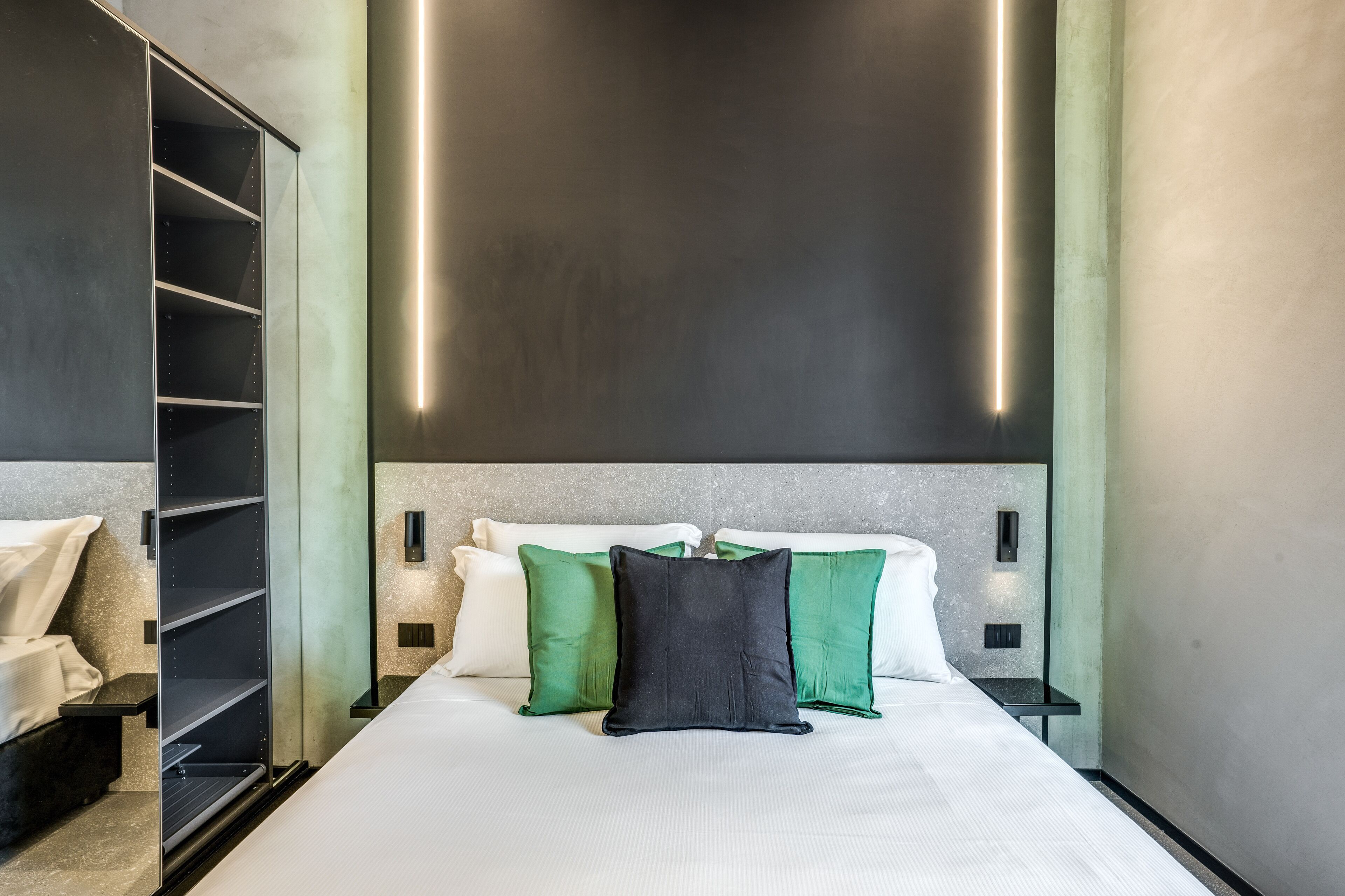Een moderne hotelkamer met een groot bed, een garderobe en inbouwverlichting.