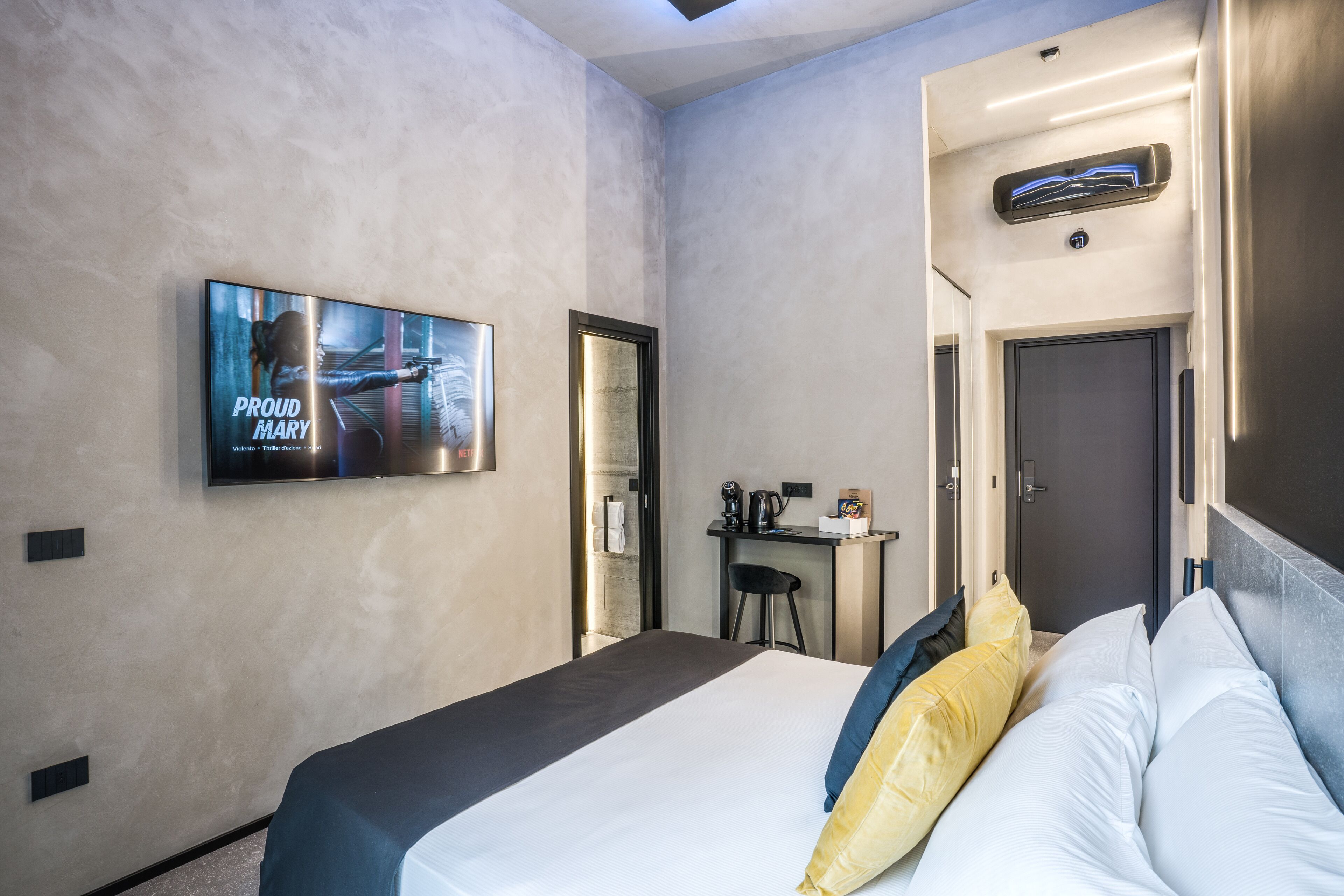 A hotel room with a bed, a TV mounted on the wall, a desk with a chair, and a door.