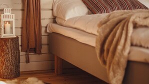 A cozy bedroom with a bed, a heart-shaped wall decoration, a hanging robe, a lantern, and a fur rug. - Tännäskröket (Tannas)