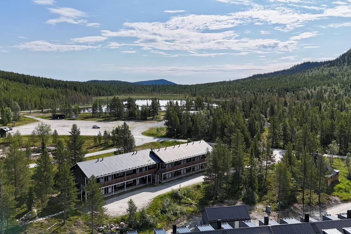 A lodge with a large building, a parking area, and a forested mountain backdrop.