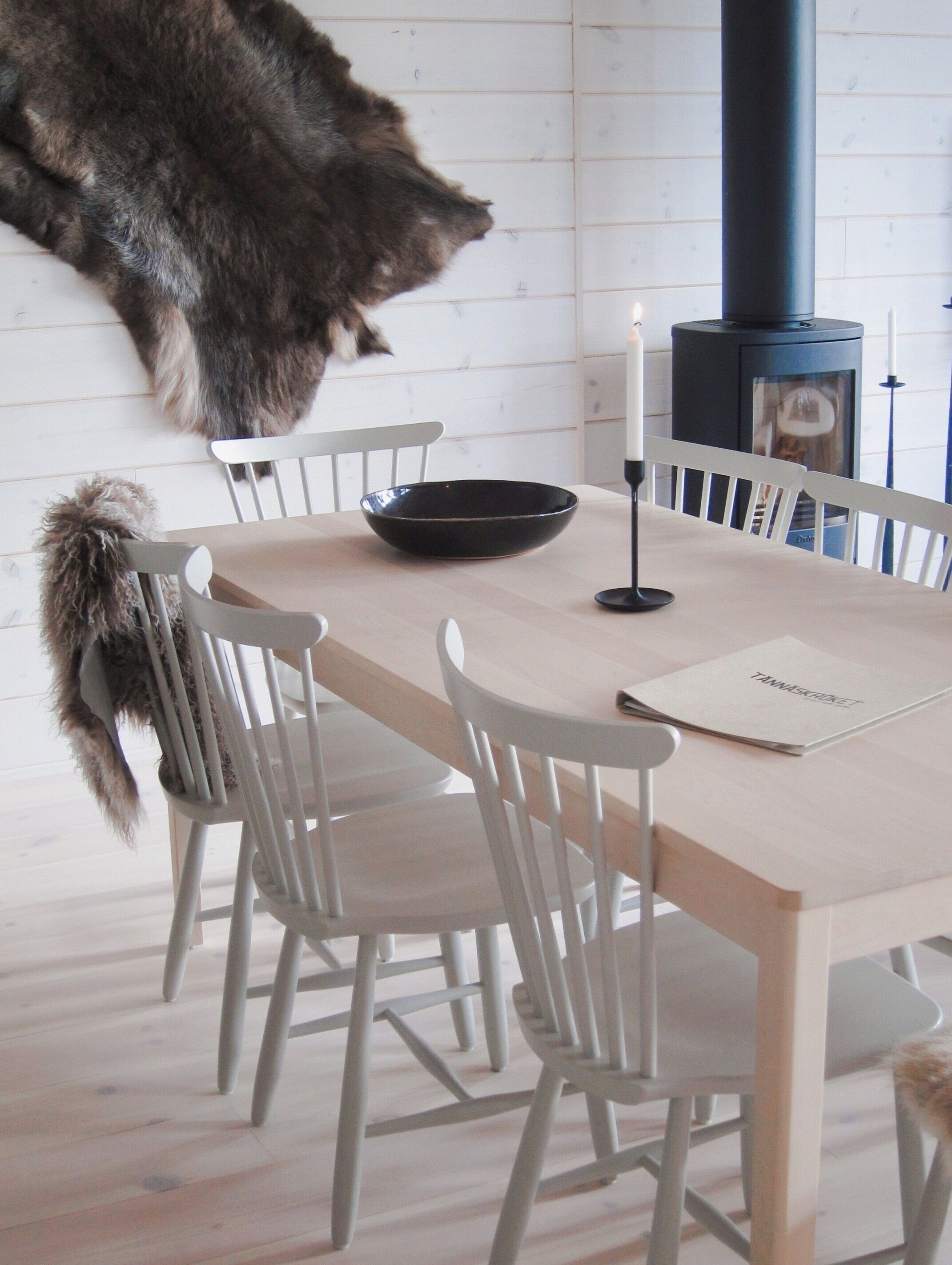 A dining area with a wooden table, white chairs, a black bowl, a candle, and a fur coat hanging on the wall.