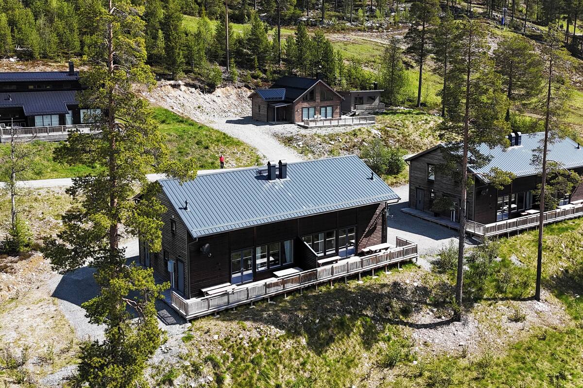 A modern lodge with a large deck, a covered patio, and a scenic mountain backdrop.