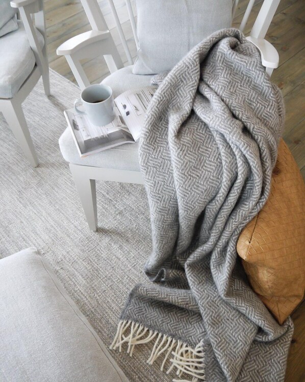 Un coin salon confortable avec un fauteuil, un coussin, une couverture et une tasse posée sur une table.