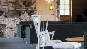 A modern lounge area with a stone wall, a white chair, a grey sofa, and a round wooden table. - Tännäskröket (Tannas)