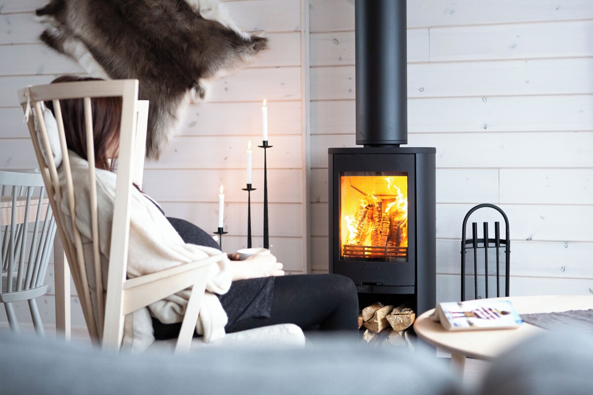 A cozy room with a wood-burning stove, a chair, and a table with a book.