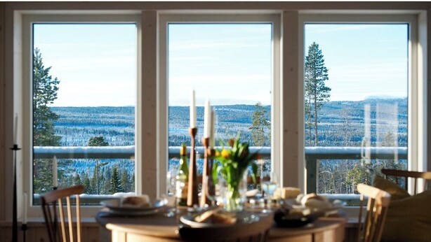 A dining area with a table set for four, large windows offering a view of a forested landscape. - Tännäskröket (Tannas)