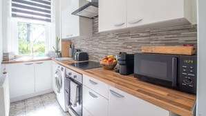 Een moderne keuken met een wasmachine, magnetron en een houten aanrecht.
