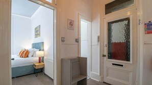 Een hotelkamer met een bed, nachtkastje, lamp en een deur met een brandmeldingsbord.