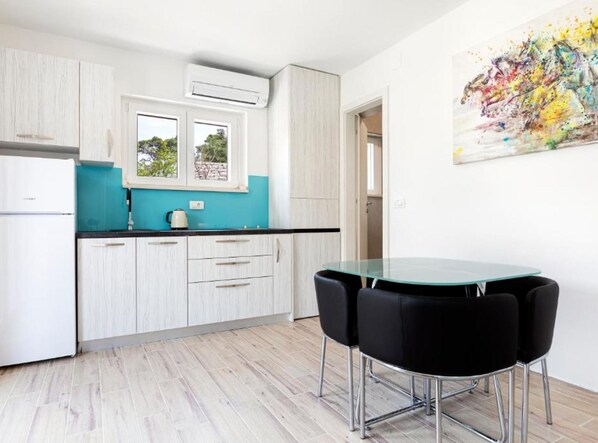 A modern kitchen with white cabinets, a teal countertop, and a glass dining table with black chairs. - White Stone House (Pucisca)