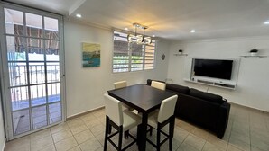 Ein Essbereich mit Tisch und Stühlen, einer Couch, einem an der Wand befestigten Fernseher und einem Wandbild.