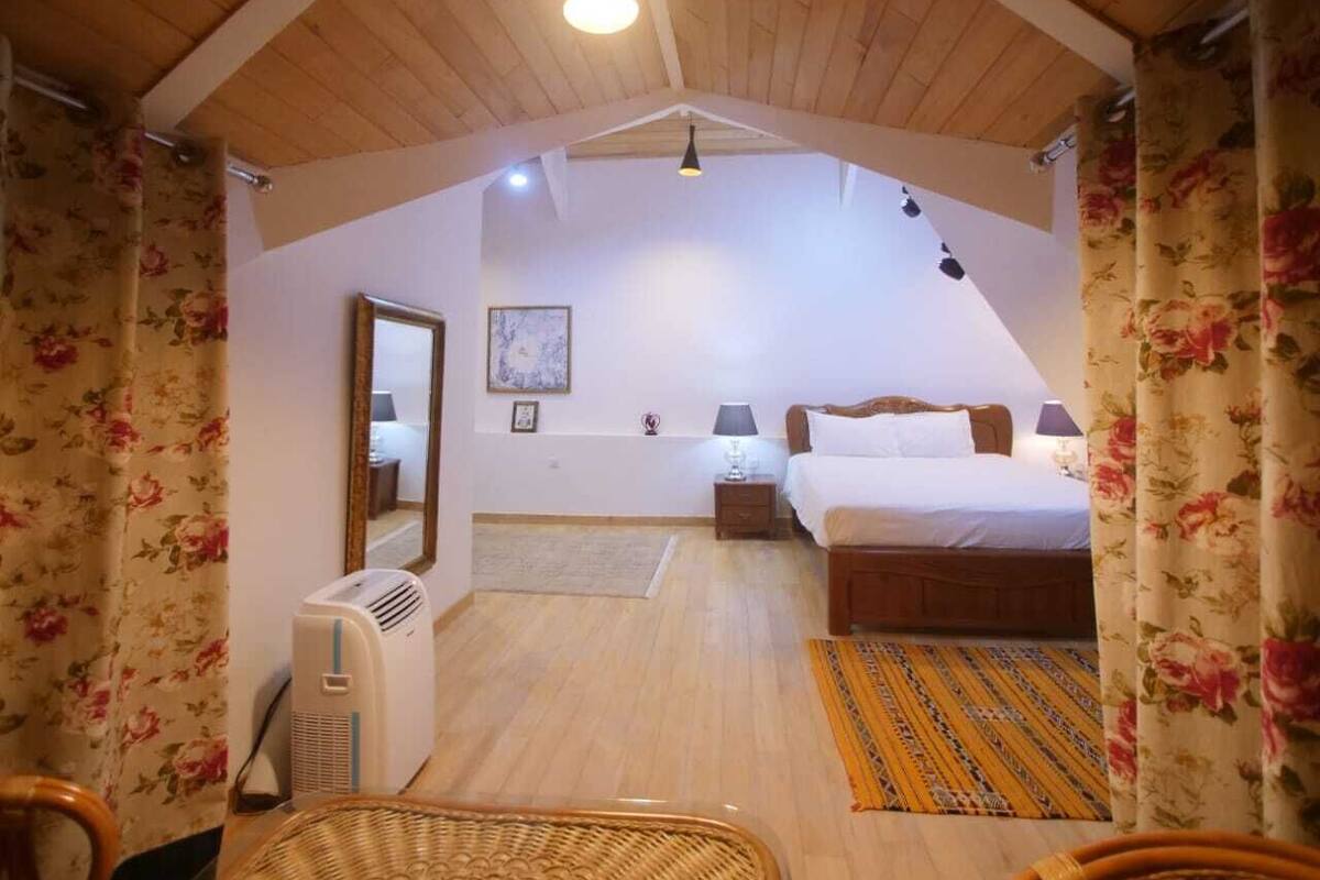 A bedroom with a wooden ceiling, a bed, a bedside table, a lamp, and a wall-mounted air conditioner.