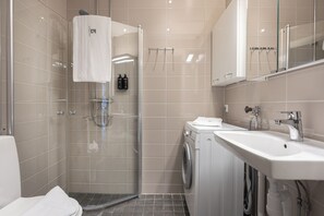 A modern bathroom with a glass-enclosed shower, a washing machine, and a sink. - HeyStay VR40 (Gothenburg)
