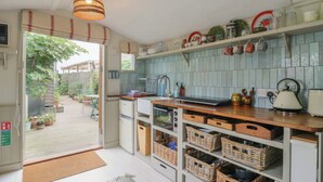 A compact kitchen with a built-in oven, a sink, and a kettle on the counter. There are baskets on the lower shelves and a hanging light fixture above. - The Artist's Cabin By The Sea (Herne Bay)