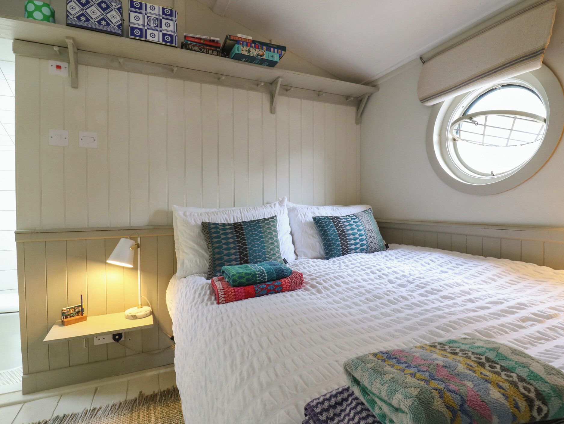 Un dormitorio acogedor con cama, almohadas, una lámpara de noche, una estantería con libros y una ventana.