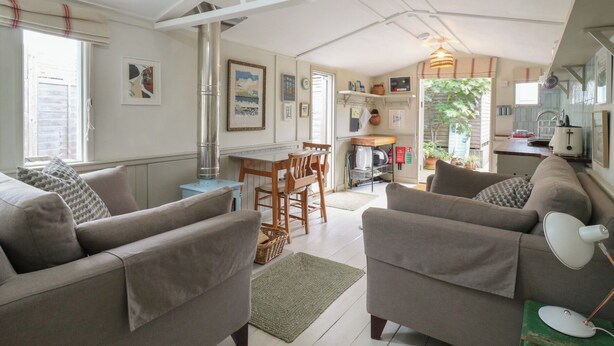 A spacious living area with a high ceiling, a dining table, and a kitchen area visible through an open door. - The Artist's Cabin By The Sea (Herne Bay)