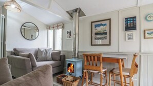 A cozy living room with a sofa, a wooden table, and a fireplace. - The Artist's Cabin By The Sea (Herne Bay)