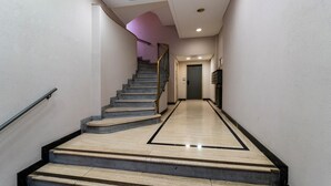 En modern hotellkorridor med en marmortrappa, ett ledstång och en dörr längst ner.