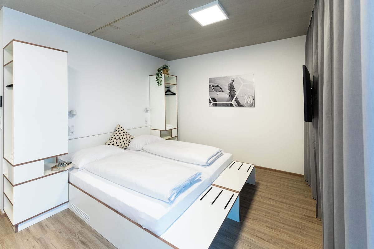 Ein modernes Schlafzimmer mit Bett, Kleiderschrank, Spiegel und einem an der Wand befestigten Fernseher.