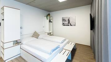 A modern bedroom with a bed, a wardrobe, a mirror, and a wall-mounted TV.