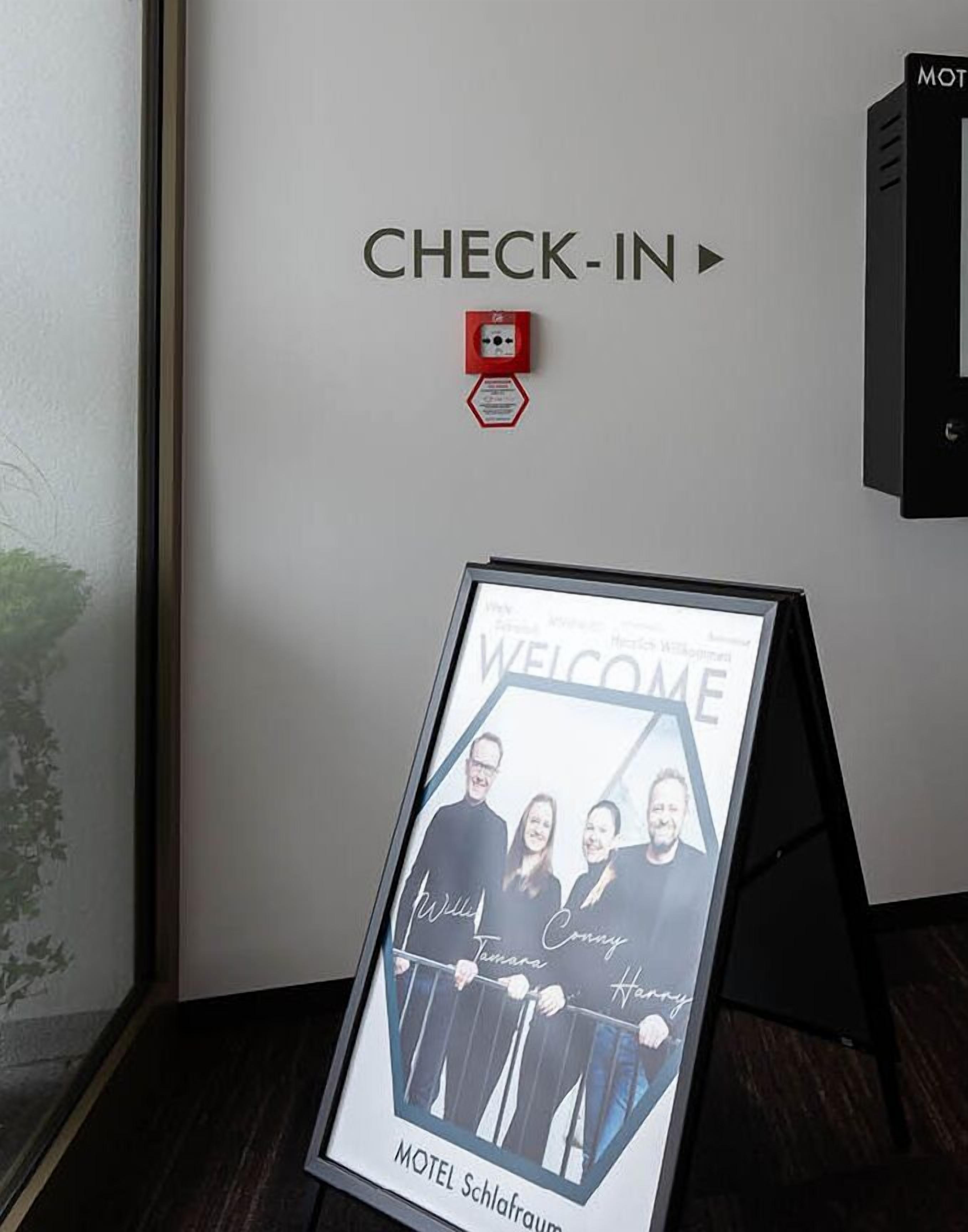 A check-in sign with a framed welcome poster and a fire alarm.