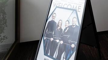 A check-in sign with a framed welcome poster and a fire alarm.