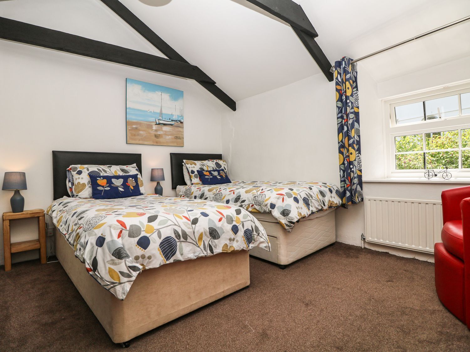 A bedroom with two beds, a window with a view, a radiator, and a red chair.